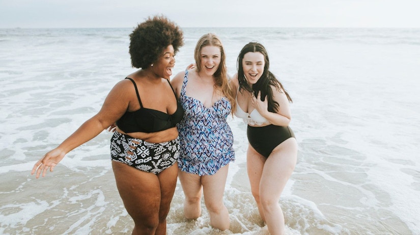 3 Frauen am Strand. Sie stehen mit den Füßen im Wasser.